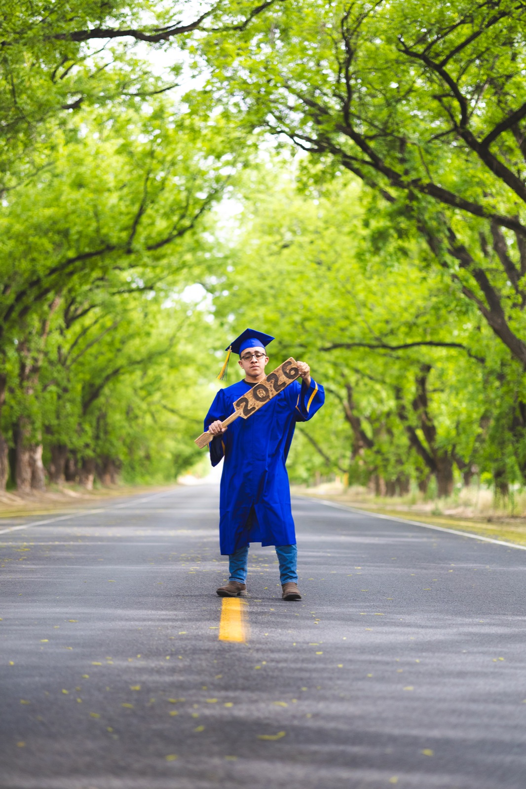 A graduate standing beneath a canopy of trees