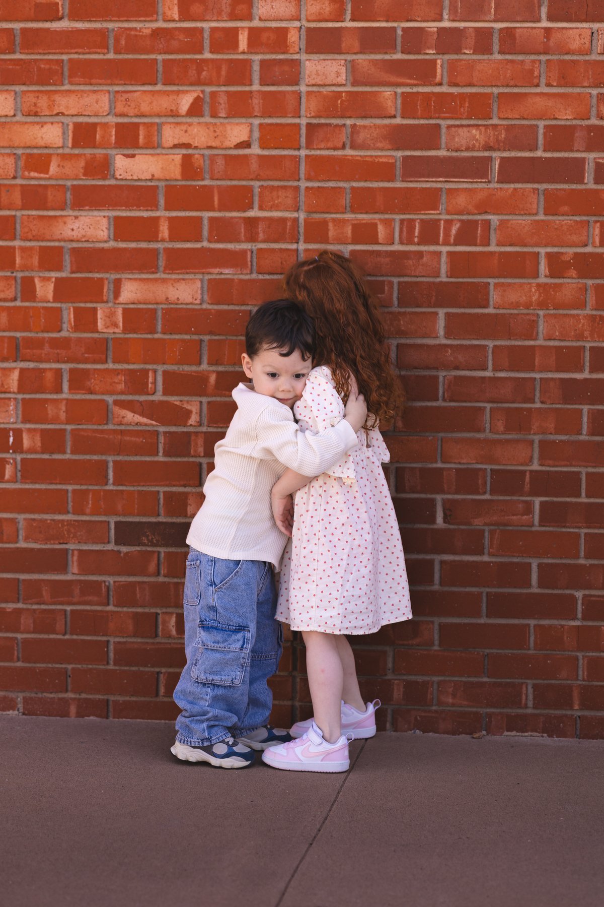 Two children hugging in front of a red brick wall