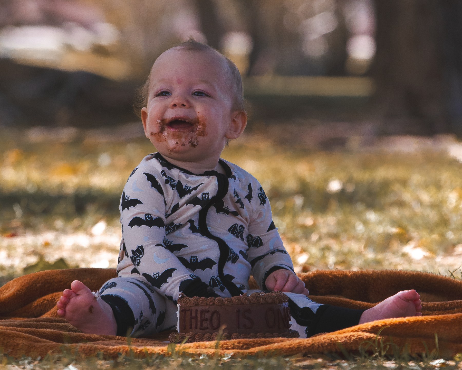 Theo sitting behind his chocolate birthday cake on a blanket outdoors