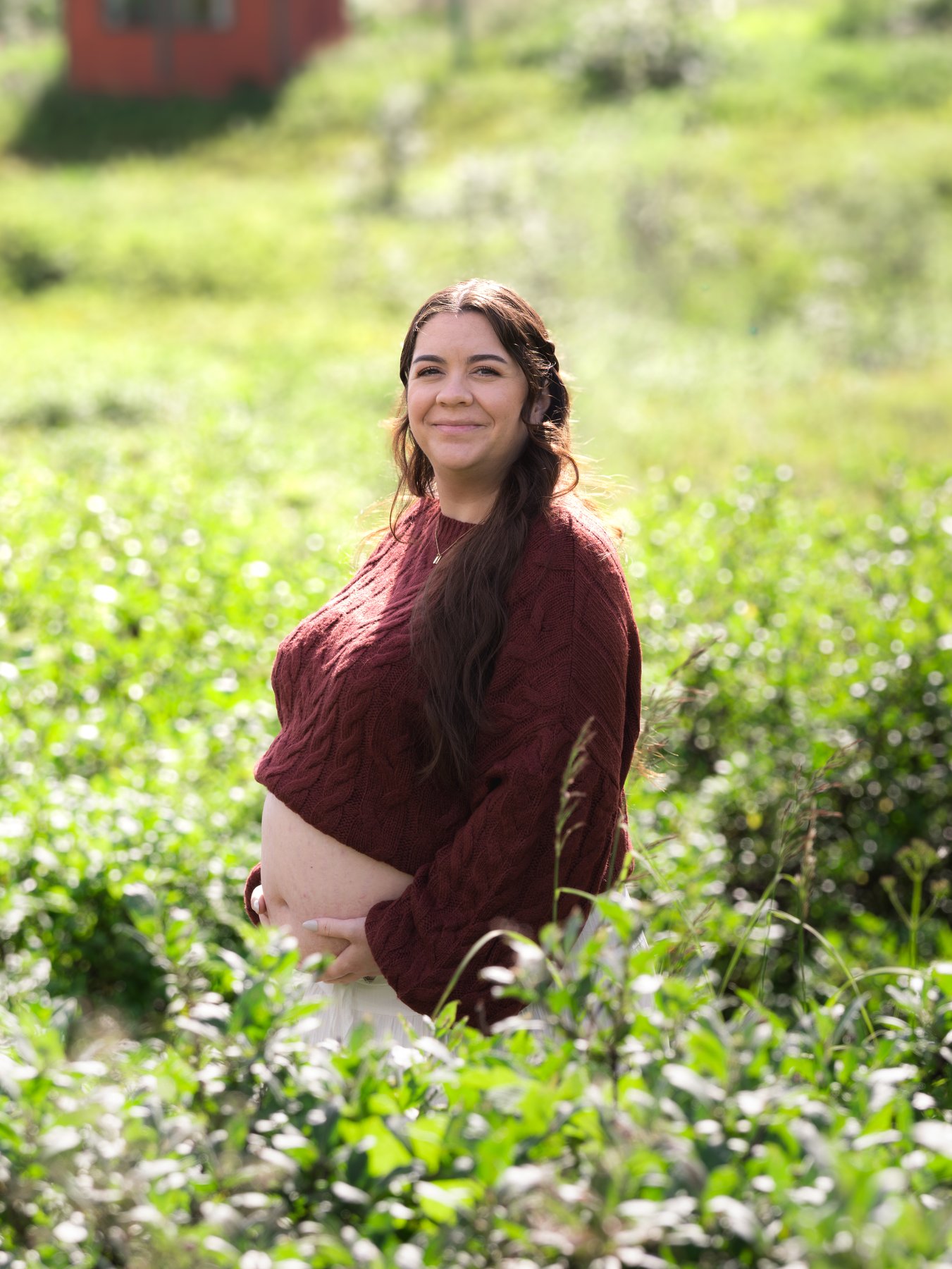 A pregnant woman standing among wildflowers with a hand beneath her baby bump