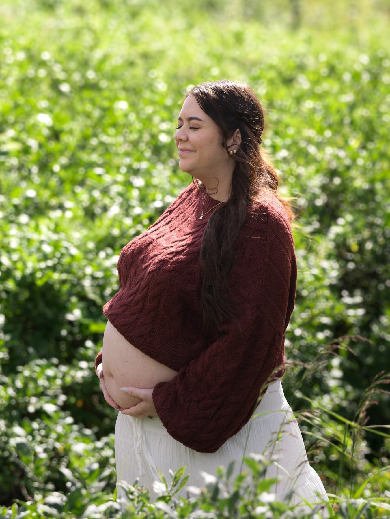 A pregnant woman in side profile, cradling her baby bump in a meadow