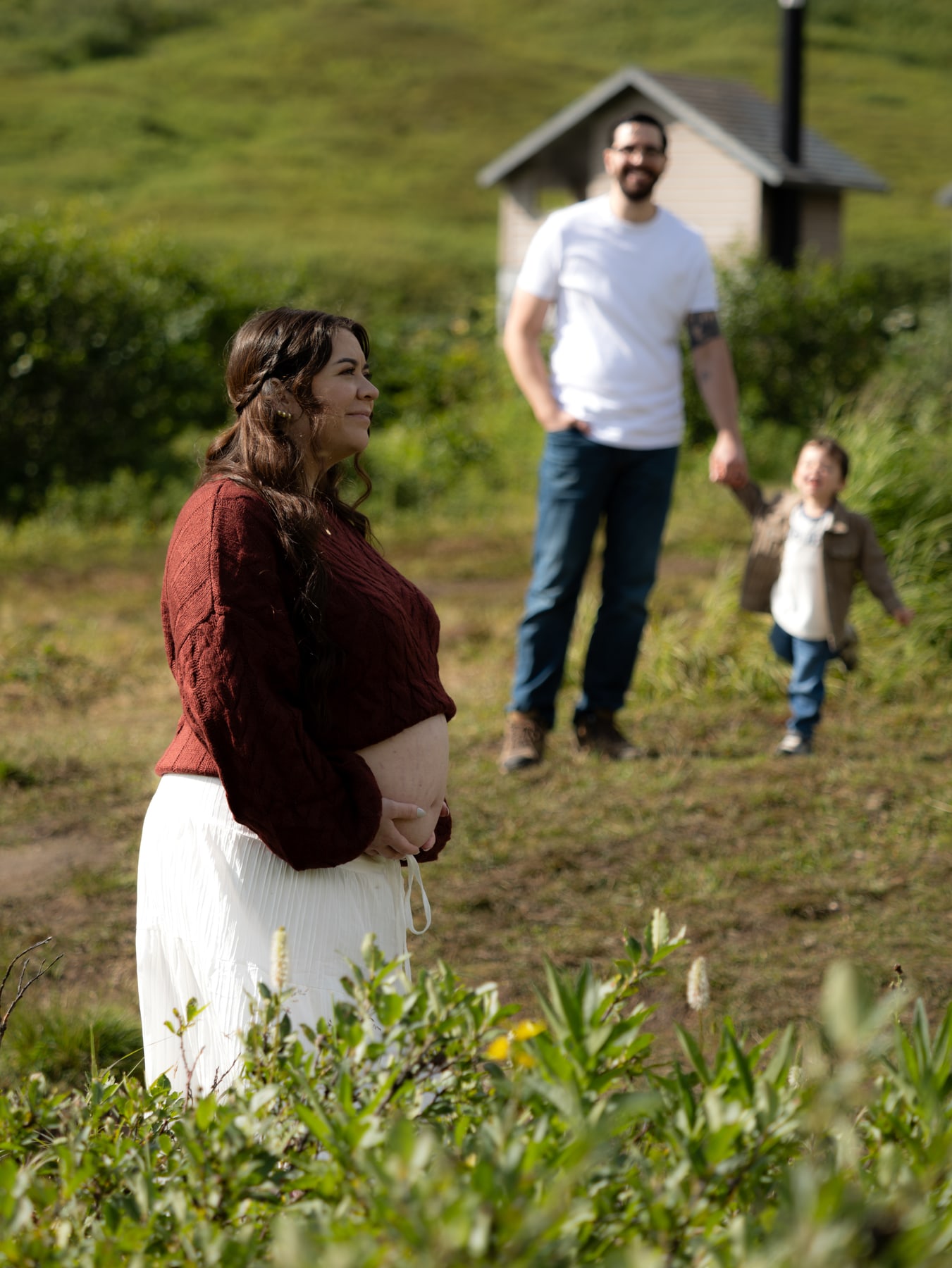 A pregnant woman cradling her baby bump, with her partner and child behind her