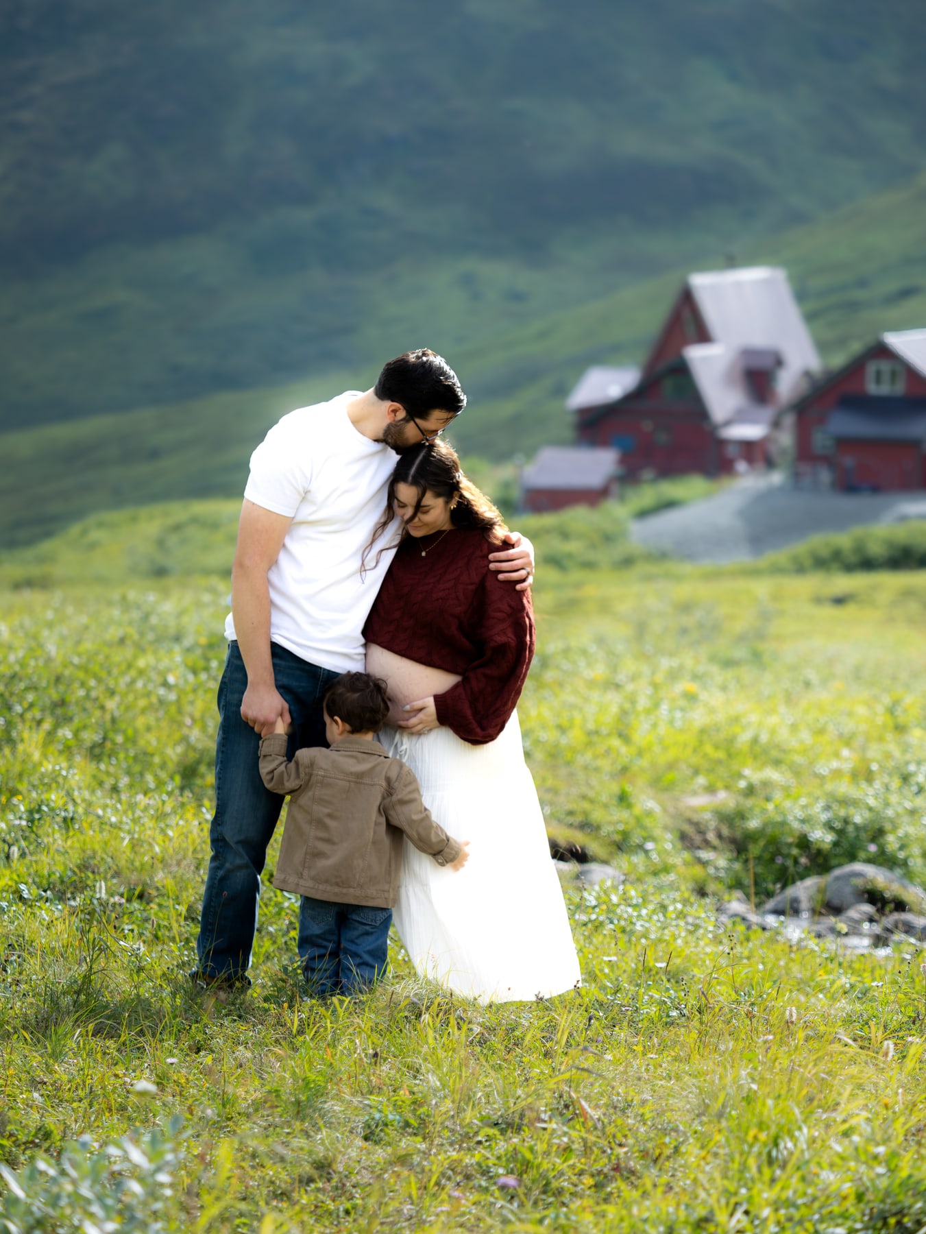 A pregnant woman, her partner and their child standing together in a green meadow