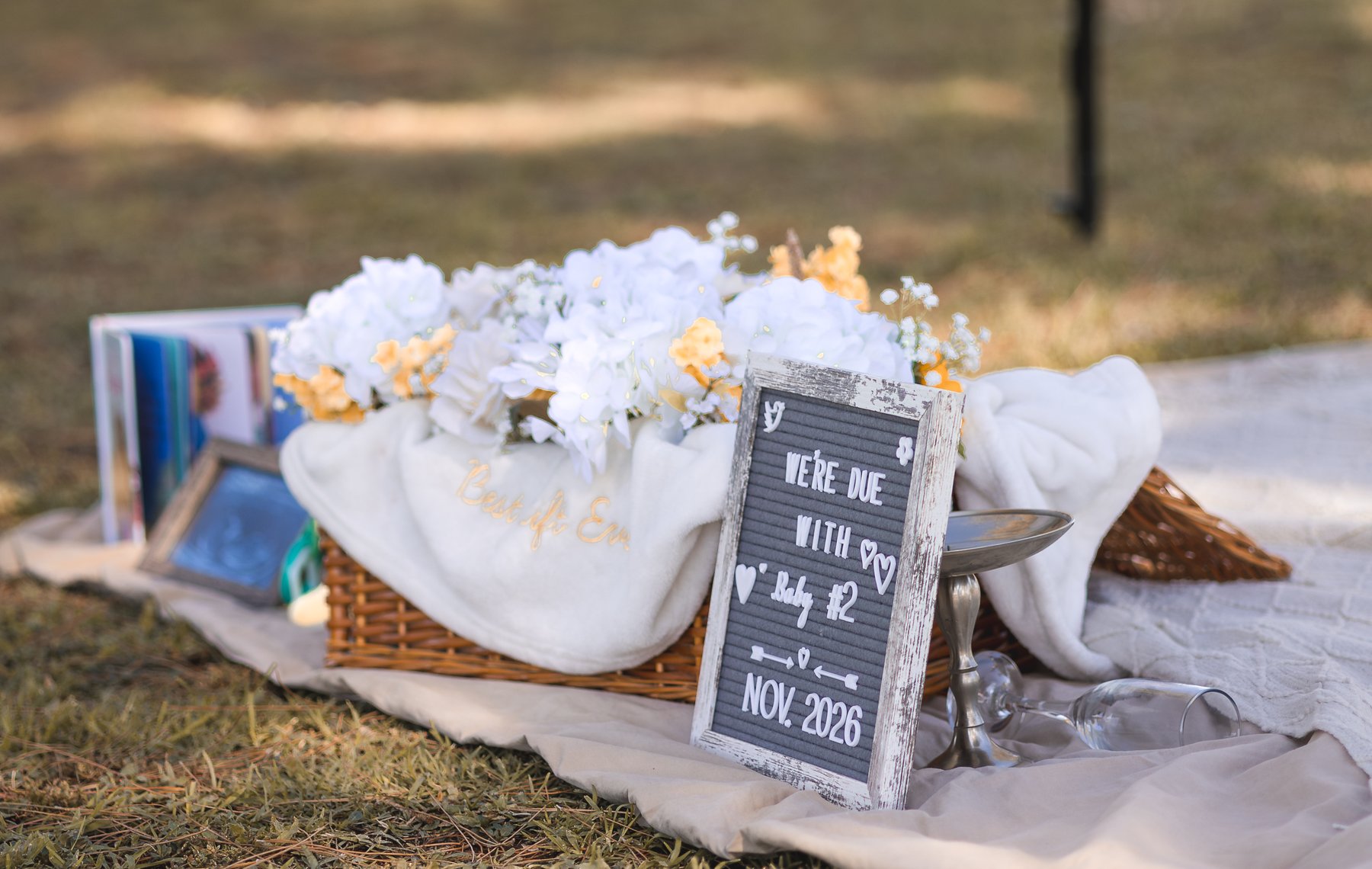 An announcement sign beside flowers and a picnic basket on a blanket