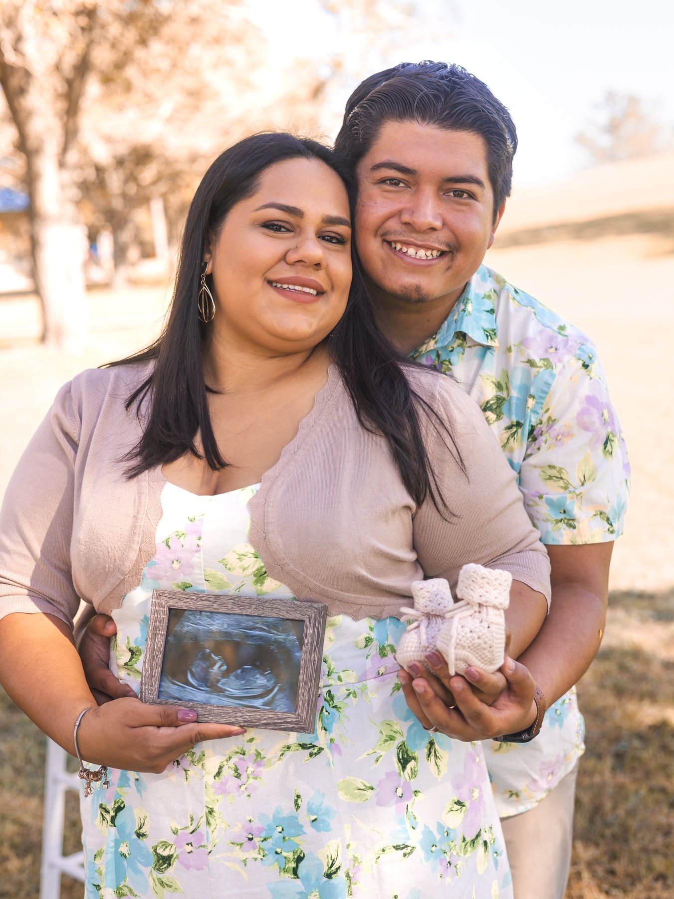 Mando and Mari holding a framed sonogram and baby shoes together