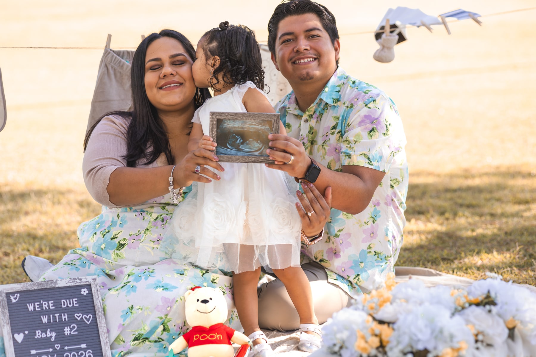 A child kissing a parent’s cheek as the family holds a framed sonogram