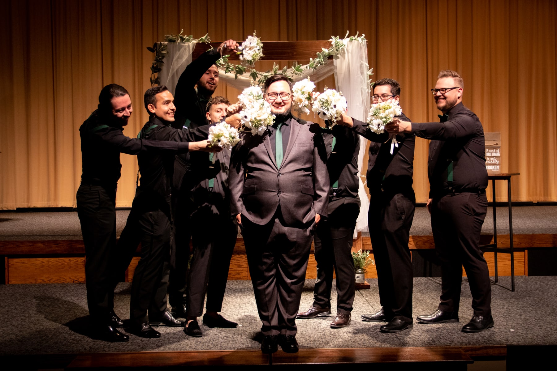 Wedding party members pointing bouquets toward the groom