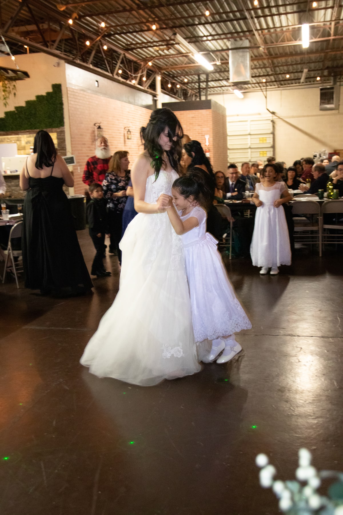 A bride dancing with a child beneath lights at her wedding reception