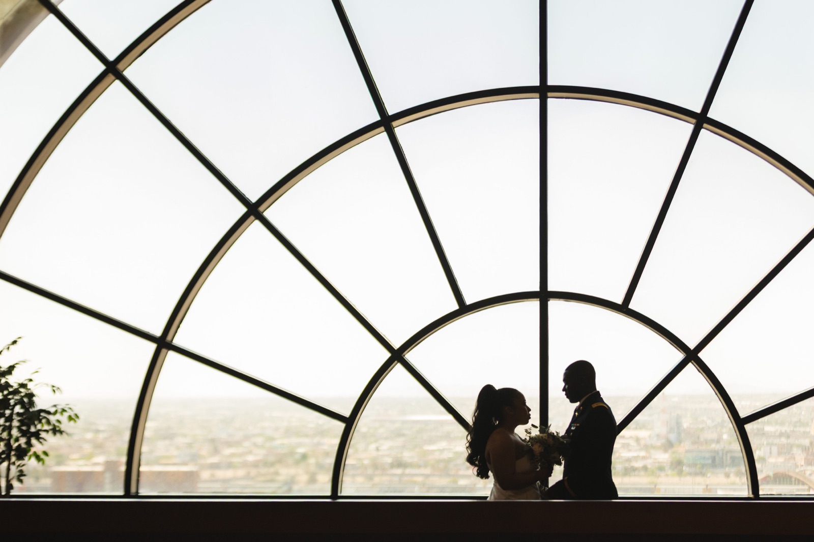 Newlyweds silhouetted beneath a large arched window