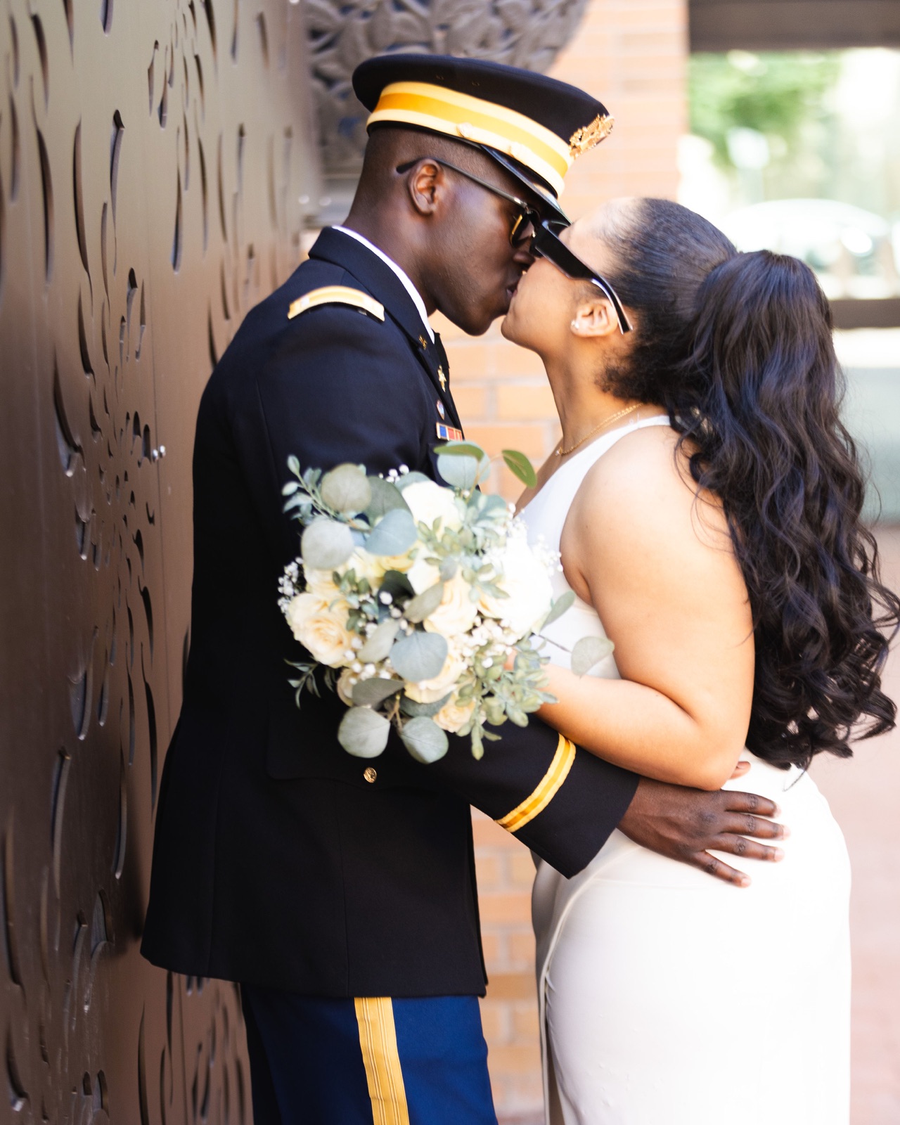 Newlyweds kissing beside a brick wall